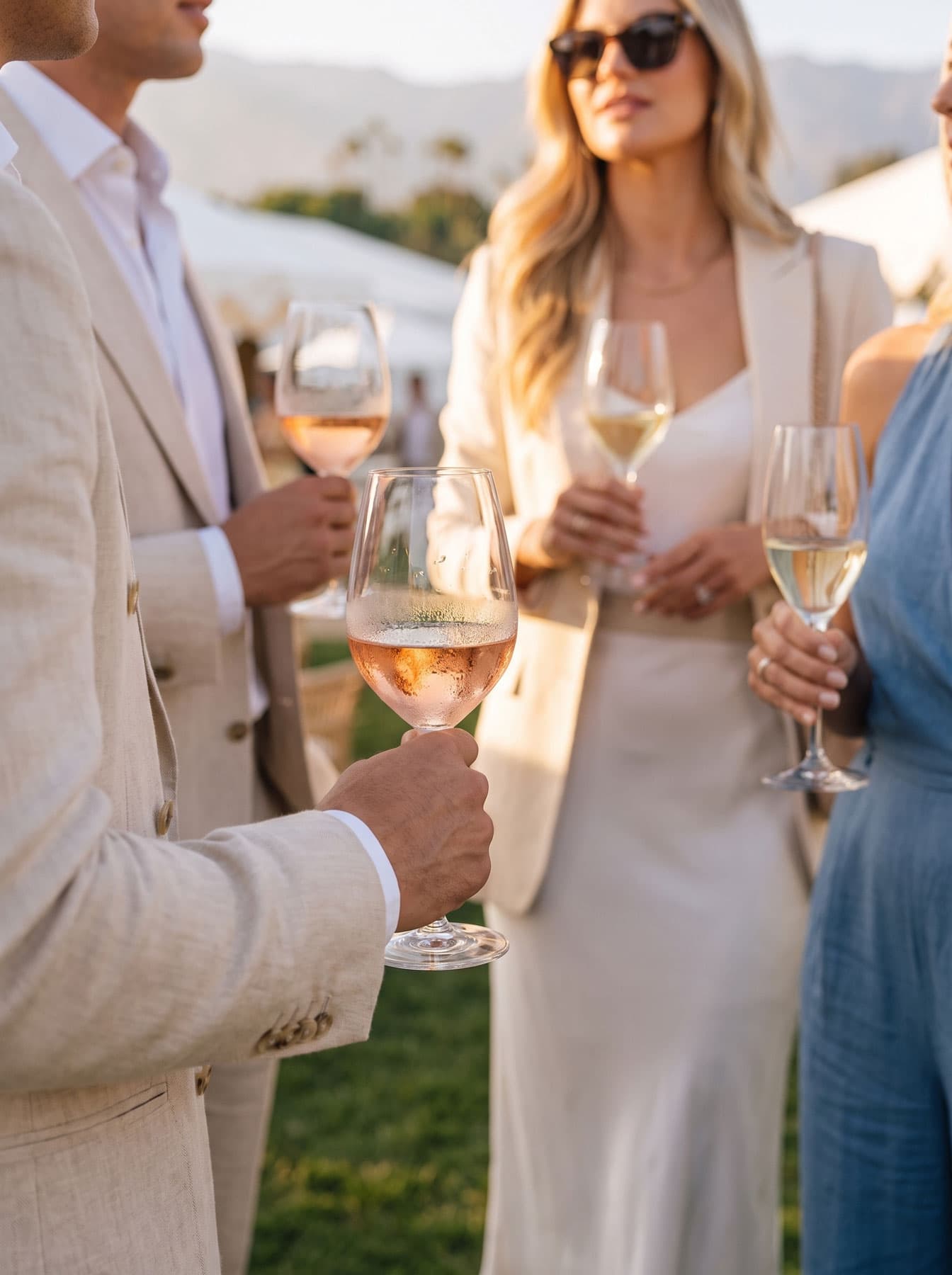Guests holding glasses of rosé and white wine on the lawn at golden hour